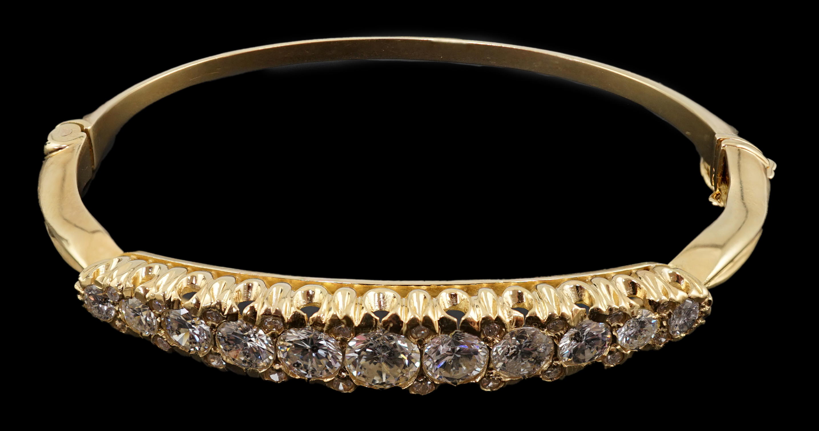 A gold and graduated eleven stone diamond set hinged bangle